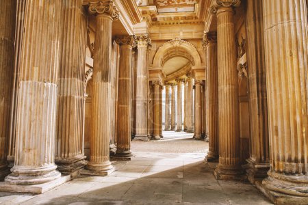 Un elegante pasillo adornado con intrincadas columnas y arcos, bañado en suave luz y sombra.