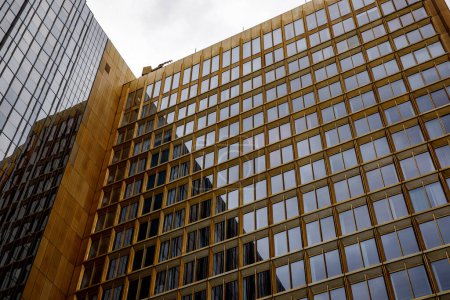 Goldfarbenes Gebäude mit reflektierenden Glasfenstern vor einer schlanken, dunkel getönten Struktur.