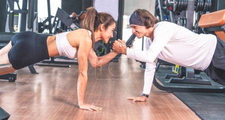 Photo for Young asian woman in sportswear with caucasian male trainer exercising together doing plank and holding hands together in gym.healthy fitness concept - Royalty Free Image