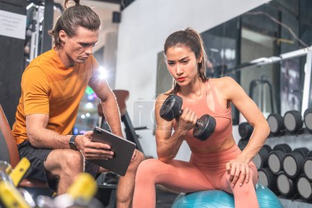Entraîneur masculin caucasien Enseigne aux jeunes femmes asiatiques de soulever des haltères pour construire des muscles du bras dans la salle de gym. Concept de fitness sain