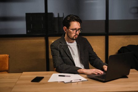 Téléchargez les photos : Jeune programmeur en costume travaille à un ordinateur dans un bureau moderne et élégant - en image libre de droit