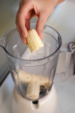 Téléchargez les photos : Femme préparant milkshake en ajoutant de la banane au mélangeur gros plan des mains - en image libre de droit