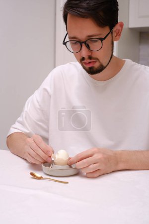 Foto de Retrato de un joven pelando un huevo en la mesa del desayuno - Imagen libre de derechos
