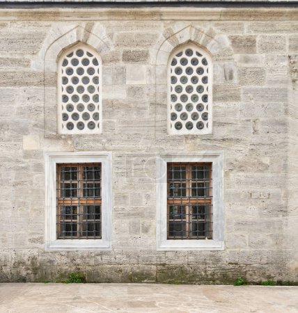 Foto de Dos ventanas de estuco arqueadas perforadas y dos ventanas con barras de hierro forjado en una pared externa de ladrillo envejecido en Mihrimah Sultan Mosque en Uskudar, Estambul, Turquía - Imagen libre de derechos