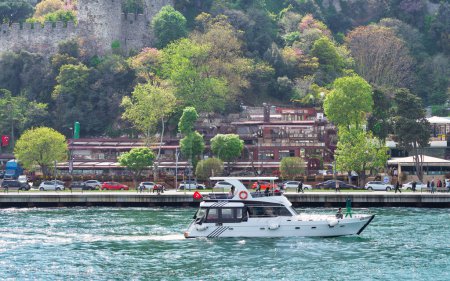 Foto de Estambul, Turquía - 8 de mayo de 2023: Barco pequeño navegando en el Estrecho del Bósforo con el distrito Rumeli Hisari al fondo - Imagen libre de derechos