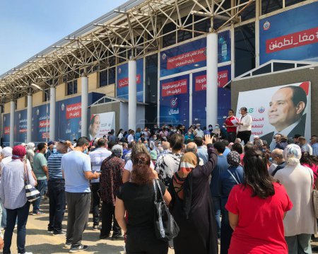 Foto de El Cairo, Egipto - 14 de agosto de 2021: Ciudadanos egipcios en el recinto ferial a la espera de su turno para recibir la vacuna contra el coronavirus Covid-19, con dos de los organizadores y antecedentes del presidente egipcio - Imagen libre de derechos