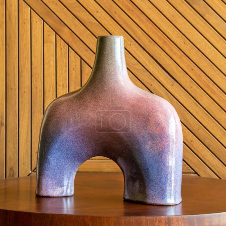 A distinctive purple and blue ceramic vase with a split-body design on a wooden table and wooden wall in the background 