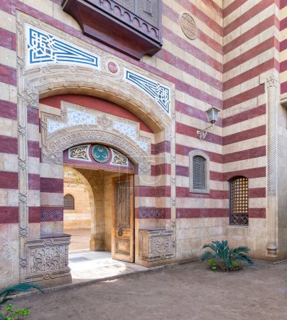 Auffällige rot-weiß gestreifte gewölbte Eingangstür führt in ein Gebäude im Stil der Mamluk-Ära, das komplexe architektonische Details präsentiert