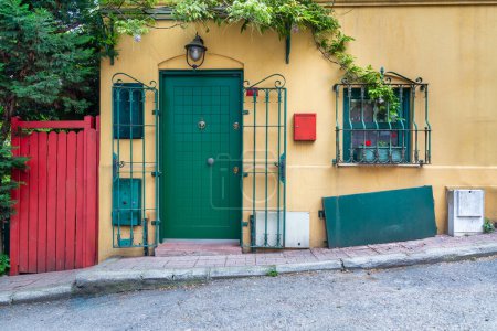 Entrée de charmante maison jaune avec porte verte et fenêtres, entourée de plantes grimpantes et de fleurs, située dans une ruelle adaptée au quartier calme de Kuzguncuk, quartier d'Uskudar, Istanbul, Turquie