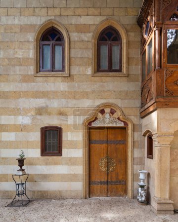 Una fachada de piedra de estilo mameluco con una puerta de madera ricamente decorada, ventanas de estilo gótico y un intrincado balcón de madera