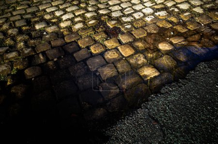 Foto de Piedras de adoquín y asfalto viejo camino superficie bajo un charco. - Imagen libre de derechos