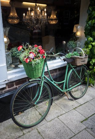 Foto de Una vieja bicicleta vintage mostrando cestas de flores fuera de una tienda de antigüedades en Gran Bretaña. - Imagen libre de derechos