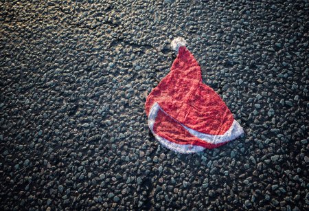 Foto de Un sombrero de Santa aplastado con marcas de neumáticos en medio de una carretera. - Imagen libre de derechos