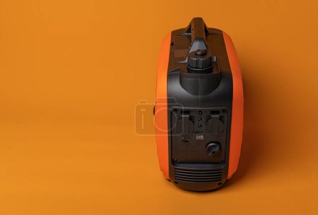 Téléchargez les photos : Electricity generator. Inverter gasoline generator on an orange background. Studio shot. - en image libre de droit