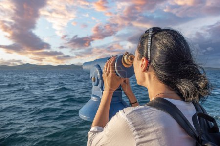 Téléchargez les photos : Une jeune femme regarde à travers un télescope au bord de la mer. - en image libre de droit