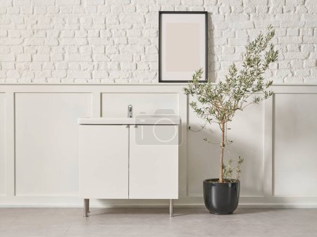 Foto de Bath room white cabinet, frame, black vase of plant olive tree, sink, white wall background. - Imagen libre de derechos
