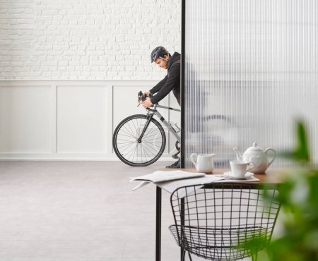 Photo for Man with bike in the room, chair table desk white brick and classic wall, blur green leaf. - Royalty Free Image