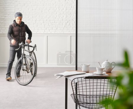 Foto de Man with bike in the room, chair table desk white brick and classic wall, blur green leaf. - Imagen libre de derechos