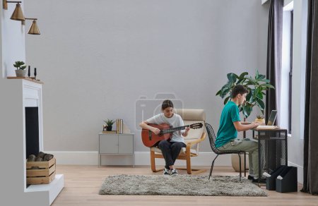 Foto de Dos hermanos hermano y hermana en la habitación, él está trabajando y ella está tocando un estilo de guitarra. - Imagen libre de derechos