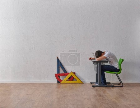 Téléchargez les photos : Adolescent concept étudiant homme dans la classe, bureau, chaise, étagère et outils géométriques sur le fond de mur gris. - en image libre de droit