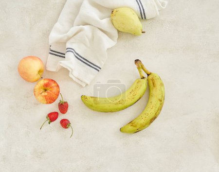 Photo for Fruits are on the table grey concrete background, banana apple and napkin, shot from above - Royalty Free Image