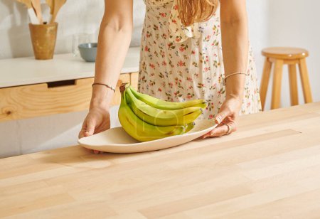 Foto de Mujer ofrece plátanos en la cocina, mesa de madera. - Imagen libre de derechos