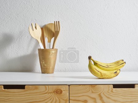 Foto de Estilo de cocina de plátano amarillo, mesa de madera, tabla de cortar agua. Tenedor y cuchara de madera. - Imagen libre de derechos