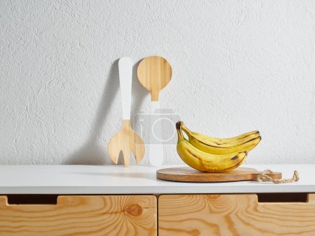 Téléchargez les photos : Banane jaune style cuisine, table en bois, planche à découper l'eau. Fourchette et cuillère en bois. - en image libre de droit