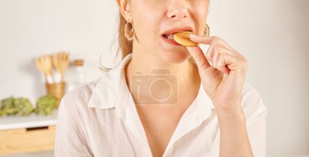 Photo for Woman eating biscuit, close-up, mouth and hand. Kitchen background style. - Royalty Free Image