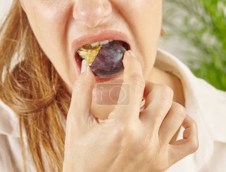 Téléchargez les photos : Femme mangeant prune, gros plan, bouche et main. Style de fond de cuisine. - en image libre de droit