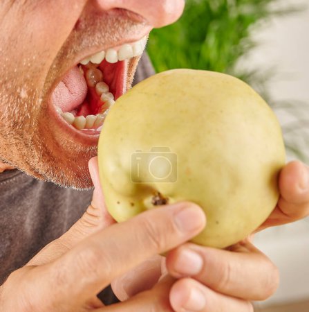 Téléchargez les photos : Fermez la bouche de l'homme qui mange de la pomme rouge. Fond de cuisine. - en image libre de droit