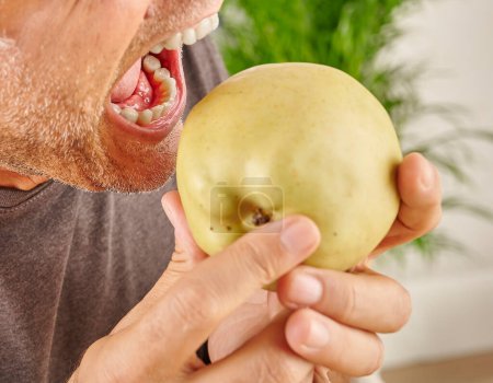 Téléchargez les photos : Fermez la bouche de l'homme qui mange de la pomme rouge. Fond de cuisine. - en image libre de droit