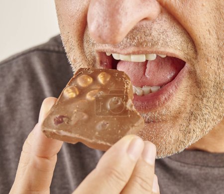 Foto de Hombre comiendo chocolate, primer plano, mano y boca. Fondo de cocina. - Imagen libre de derechos