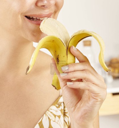 Téléchargez les photos : Femme mangeant de la banane, gros plan, main et bouche. Fond de cuisine. - en image libre de droit
