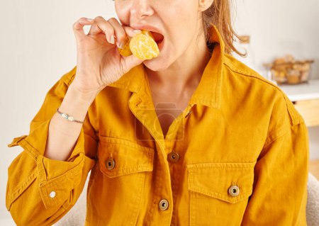 Foto de Mujer comiendo mandarina, primer plano, mano y boca. Fondo de cocina. - Imagen libre de derechos