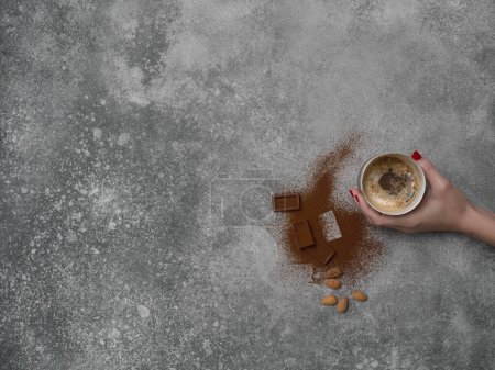 Foto de Cerámica de vidrio estilo café, chocolate y almendras en el fondo de la mesa de piedra, estilo decorativo gris. Mujer mano. - Imagen libre de derechos
