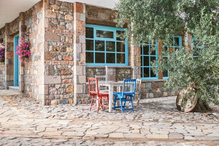 Photo for Stone house, decorative window, garden, wooden chair and table, olive-tree, outside. - Royalty Free Image
