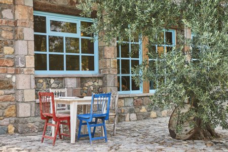 Foto de Casa de piedra, ventana decorativa, jardín, silla y mesa de madera, olivo, exterior. - Imagen libre de derechos