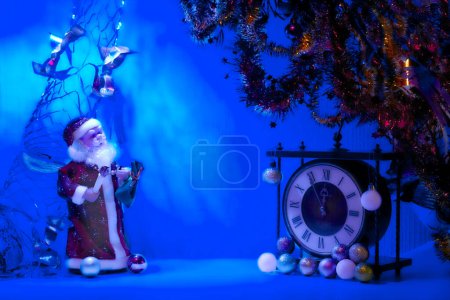 Téléchargez les photos : La fête chrétienne annuelle célébrant la naissance des Christs, qui a eu lieu le 25 décembre dans l'Église occidentale. Père Noël en lumière bleue et horloge vintage. Nouvel An jouets de Noël, guirlandes. - en image libre de droit