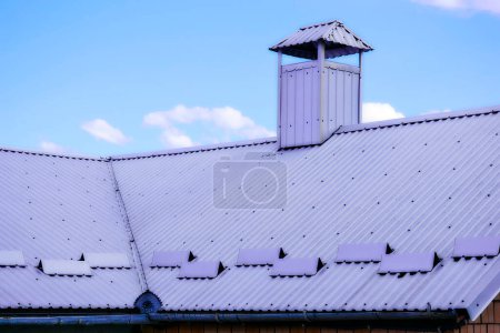 Gray silver metal tile profile on the roof of a house and blue clear sky                               
