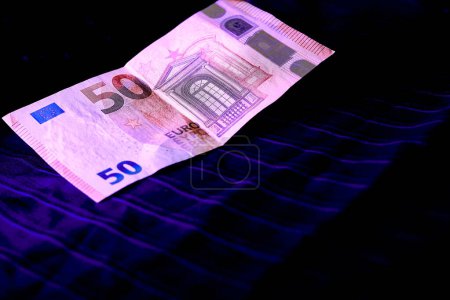 Money. 50 euro banknote being examined under ultraviolet light on a dark cloth                               