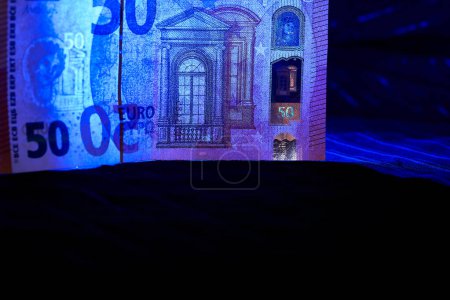 Money. 50 euro banknote being examined under ultraviolet light on a dark cloth                               