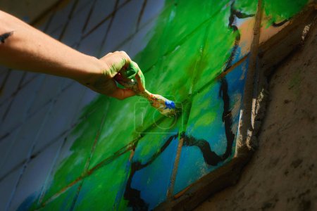 Female artist's hand with a brush painting graffiti on the wall                                