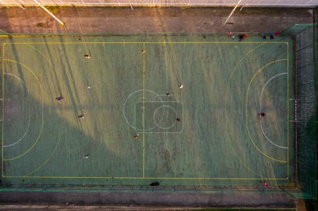 Aerial drone top view of mini football soccer field with artificial plastic cover with playing people. Public sport ground in city at sunny summer day drone view. Mini soccer field for children