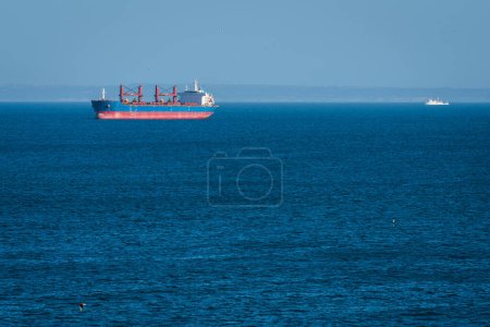 Blaues ruhiges Wasser des Ozeans und Schiffe in der Ferne vor dem nebligen Horizont, selektiver Fokus.