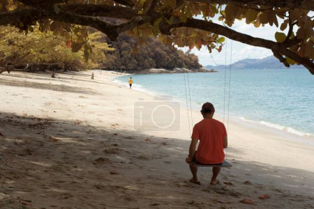 Photo for Infrared image of an unknown man sitting alone on the single rope bench swing under the tree - Royalty Free Image