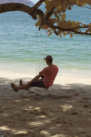 Photo for Infrared image of an unknown man sitting alone on the single rope bench swing under the tree - Royalty Free Image