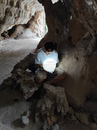 Téléchargez les photos : Modèle masculin tenant une boule de cristal brillant dans la main à l'intérieur de la grotte sombre. - en image libre de droit