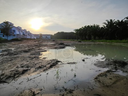 escena de una piscina reflectante vacía de tierra pluvial fangosa estancada junto a la zona residencial.