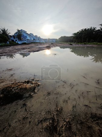 escena de una piscina reflectante vacía de tierra pluvial fangosa estancada junto a la zona residencial.